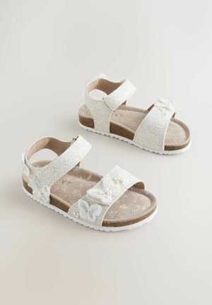 Kimaltelevat valkoiset sandaalit, joissa on kaksi säädettävää remmiä, koristeltu perhosen ja helmen koruilla pehmustetulla pohjallisella. Valkoinen kumipohja.