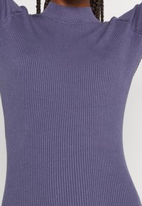 Top viola a coste con collo alto e forma aderente, caratterizzato da un tessuto testurizzato che aumenta l'interesse visivo.