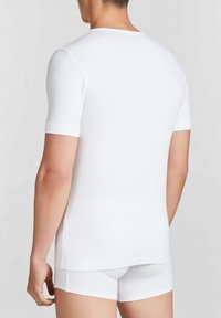 T-shirt bianco a maniche corte realizzato in tessuto liscio, con collo rotondo senza cuciture e design aderente, con biancheria intima bianca coordinata visibile.