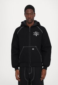 Black hooded sweatshirt made of fleece with white stitching. Features an ice cream skull graphic on the chest and front pockets.