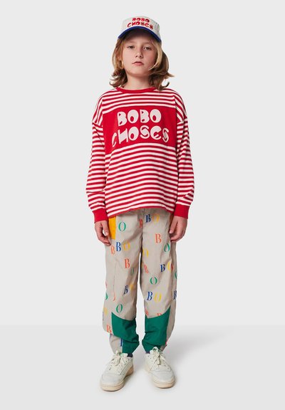 Rood-wit gestreept T-shirt met lange mouwen met de tekst "BOBO CHOSES", gecombineerd met lichtgekleurde broek met multikleuren "B"-patronen en groene accenten.