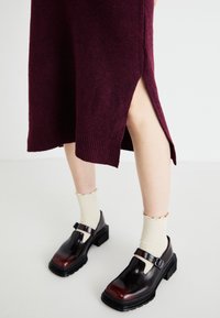 Burgundy knit dress with side split, paired with shiny black-and-burgundy shoes and cream ribbed socks with a scalloped edge.