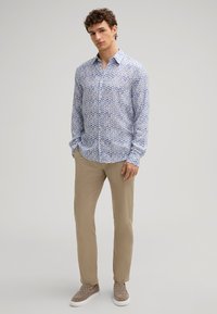 Camicia azzurra chiara con bottoni, caratterizzata da un motivo geometrico, abbinata a pantaloni beige chiaro e scarpe slip-on grigio texturizzate.