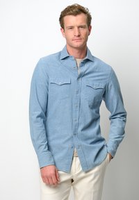 Lichtblauwe overhemshirt, lange mouwen, twee borstzakken, drukknoopdetails, gemaakt van textuurstof, gecombineerd met crèmekleurige broek.