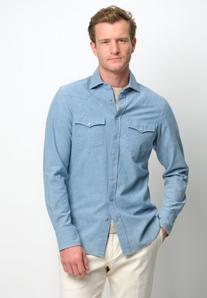 Camicia button-up azzurro chiaro, maniche lunghe, due tasche sul petto, dettagli con bottoni a scatto, realizzata in tessuto testurizzato, abbinata a pantaloni color crema.