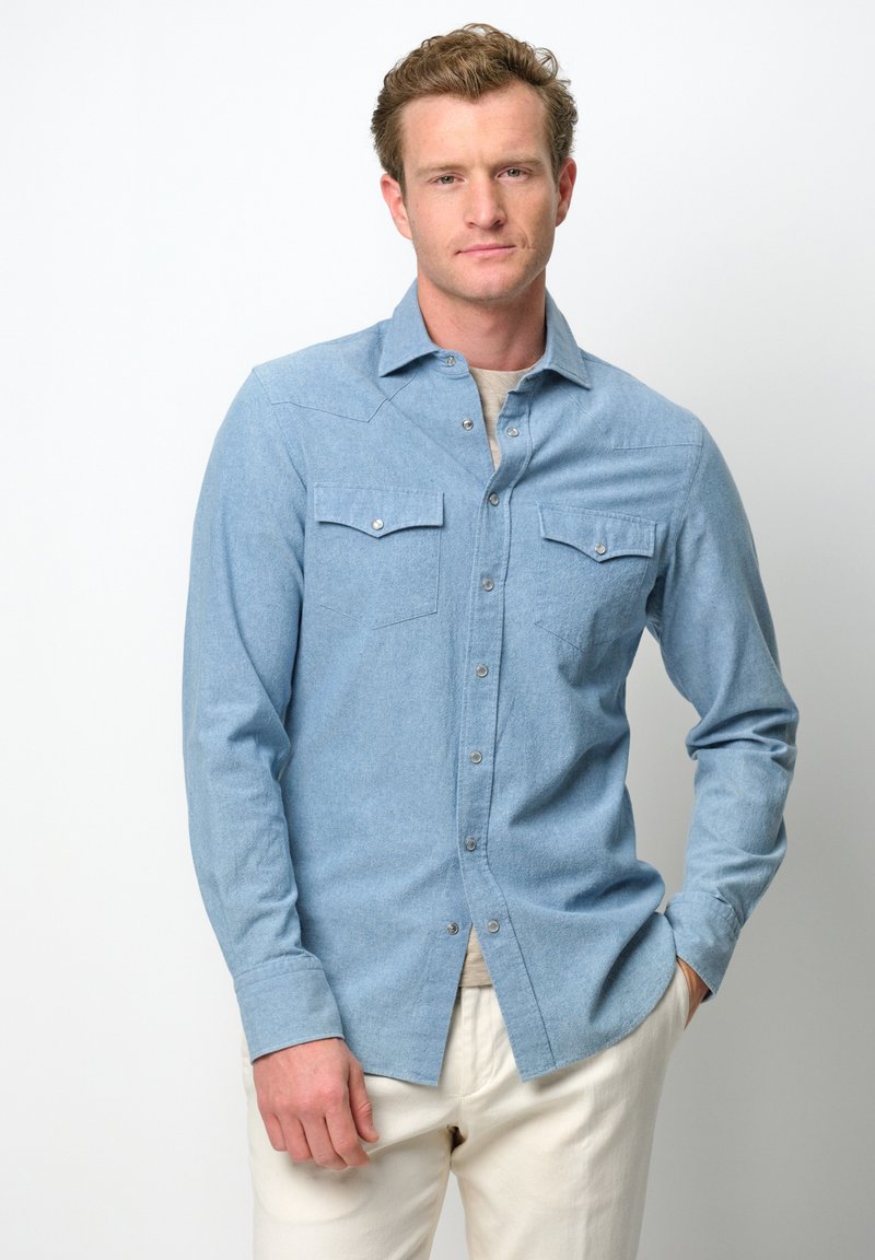 Lichtblauwe overhemshirt, lange mouwen, twee borstzakken, drukknoopdetails, gemaakt van textuurstof, gecombineerd met crèmekleurige broek.