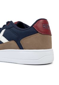 Zapatilla de lona azul marina con detalles de ante marrón, suela de goma blanca y un tirador de talón de cuero rojo. Presenta una prominente franja de logo blanca en el lateral.