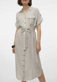 Abito midi a righe in beige chiaro con linee verticali. Presenta una scollatura a V, una chiusura con bottoni, due tasche sul petto e una cintura legata in vita.