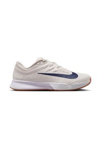 Chaussure de sport beige clair avec une tige texturée, logo swoosh bleu foncé, semelle intermédiaire blanche et semelle extérieure en caoutchouc gomme. Lacets et onglet au talon inclus.