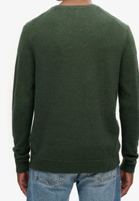 Pull en laine vert avec un col rond et un ourlet côtelé. Doté de manches longues et d'un tissu doux et texturé. Porté avec un jean bleu clair.