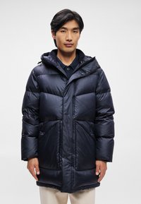 Casaco puffer azul-marinho com capuz, apresentando fecho de correr, grandes bolsos frontais e punhos canelados. Feito de material brilhante e isolante.