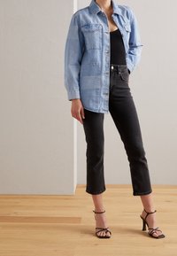 Světle modrá džínová bunda s patchworkovým designem, má límec a knoflíkový přední zapínání, v kombinaci s černými zkrácenými džíny a černými páskovými podpatky.