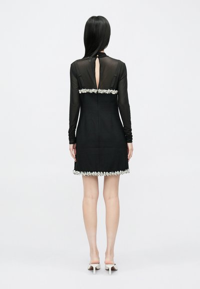 Melnas kleitas ar caurspīdīgu garu piedurkņu augšdaļu, atvērumu muguras daļā un izrotātu ziedu apdari gar apakšmalu. Gluda auduma un pieguloša dizaina.