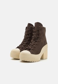 Brown suede high-top shoes with a cream rubber toe cap and chunky platform heel. Features lace-up design and textured sole for grip.