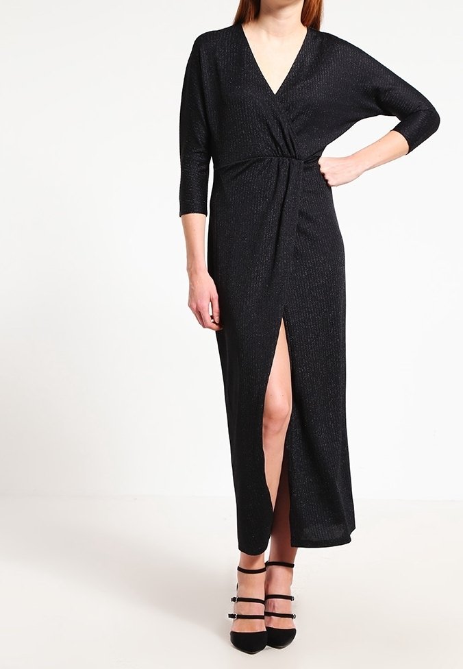 Femme portant une robe midi noire à manches longues de style portefeuille avec une fente devant et des chaussures à talons hauts noires à brides.