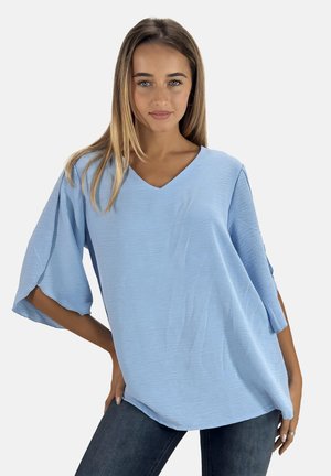 Light blue oversized V-neck blouse with short sleeves, featuring a textured fabric and loose fit. Paired with dark jeans.