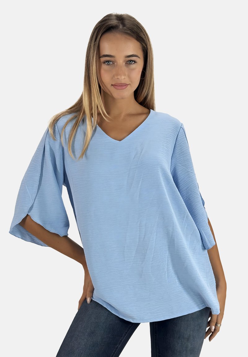 Lichtblauw oversized V-halsblouse met korte mouwen, gemaakt van een textiel met structuur en een losse pasvorm. Gecombineerd met donkere jeans.