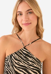 Top halter con stampa zebra nera e crema con spalline incrociate. Il tessuto morbido, la consistenza liscia e la vestibilità rilassata mettono in risalto il design.