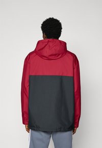 Rød og mørkegrå sporty jakke med hette, med delt-farge design og elastisk midjebånd, laget av lett stoff.