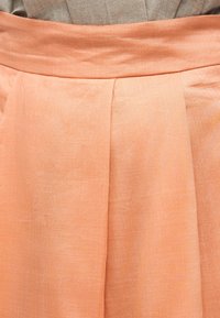 Φούστα από λινό σε ροδακινί χρώμα με ψηλή μέση και πιέτα στο μπροστινό μέρος πάνω σε ουδέτερο υφασμάτινο φόντο.