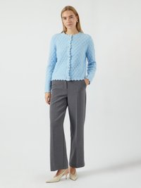 Cardigan tricoté bleu clair avec un motif en diamant texturé, des bords festonnés et de gros boutons ; associé à un pantalon large gris et des talons beiges.