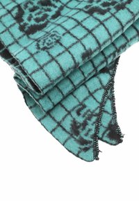 Coperta di lana turchese con un motivo a griglia nera, caratterizzata da bordi sfilacciati e una texture morbida, piegata per mostrare i dettagli.