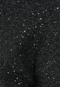 Tissu tricoté noir avec de petites paillettes brillantes éparpillées créant une texture subtilement scintillante.