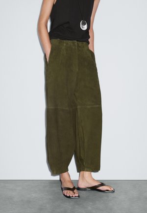 Olijfgroene suede wijde broek met zakken, gekenmerkt door een gladde textuur en een ontspannen pasvorm, gecombineerd met zwarte minimalistische flip-flops.