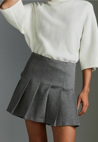 Gonna grigia plissettata realizzata in tessuto con una finitura testurizzata, abbinata a un maglione bianco in maglia spessa con scollo alto.