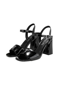 Sandales à talons hauts en cuir verni noir avec bout ouvert, bride de cheville réglable et accents métalliques décoratifs à l'avant.