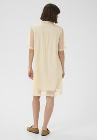 Durchsichtiges gelbes Spitzekleid mit kurzen Ärmeln, Kragen und knielangen Schnitt. Verfügt über eine lässige Passform und zarte Textur. Leichtes und luftiges Design.