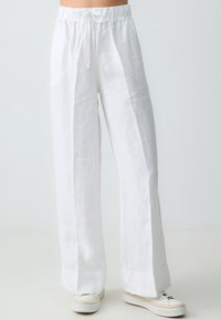 Pantalons larges en lin blanc avec une taille élastique et deux coutures frontales. Présente une coupe décontractée et un tissu lisse légèrement texturé.
