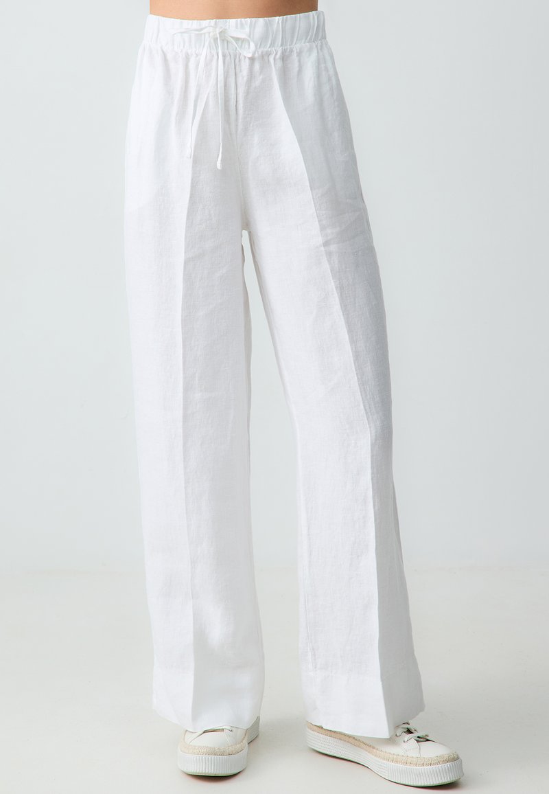 Pantalons larges en lin blanc avec une taille élastique et deux coutures frontales. Présente une coupe décontractée et un tissu lisse légèrement texturé.