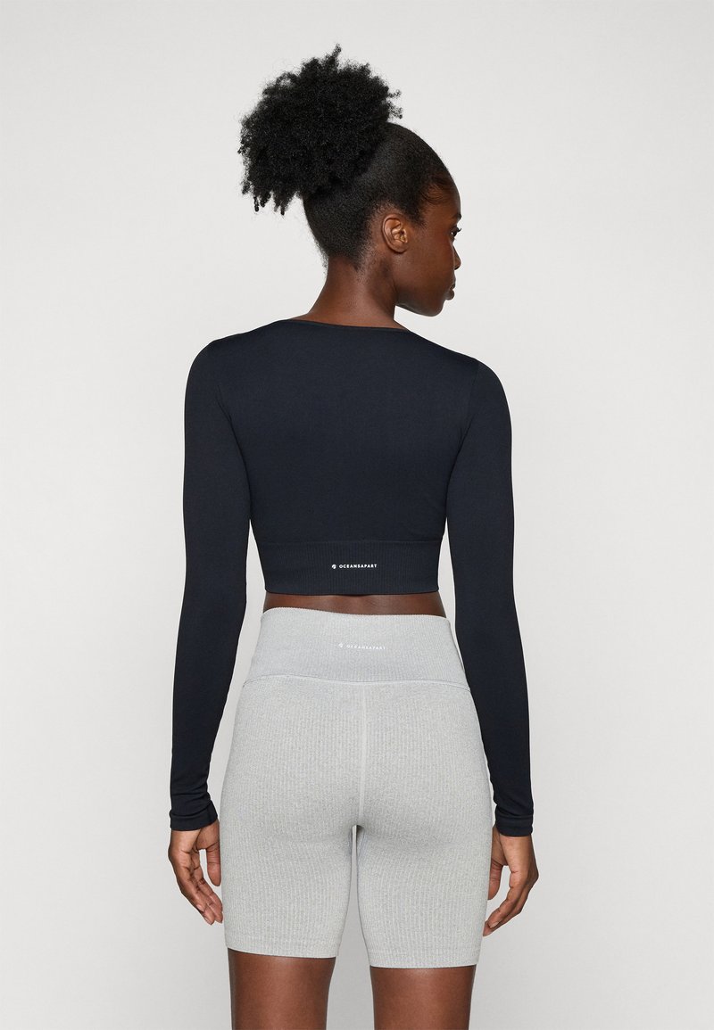 Czarny długi rękaw crop top o dopasowanym kroju, w parze z jasnoszarymi, teksturowanymi szortami rowerowymi, oba z subtelnym logo.