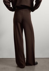 Brown wide-leg pants made from soft material, featuring a relaxed fit with a high waistband. Smooth texture with no visible patterns.