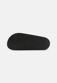 Black shoe sole featuring a textured hexagonal pattern, smooth edges, and a rounded toe for grip and comfort.