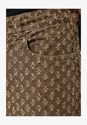 Tessuto denim marrone con motivo ricamato in rilievo di piccole figure su tutta la superficie. Presenta una tasca frontale e un design standard della vita.