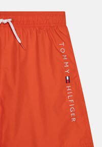 Costume da bagno arancione realizzato in tessuto leggero con vita elasticizzata, lacci bianchi e logo del brand ricamato di lato.