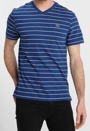 Niebieska koszulka V-neck z białymi poziomymi paskami, krótkimi rękawami i małym zielonym akcentem logo na lewej piersi. Materiał bawełniany.