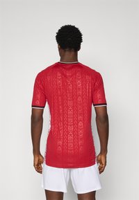 Rood T-shirt met korte mouwen, voorzien van een textuurpatroon en witte accenten langs de zijkanten. De kraag heeft een contrasterende bies.