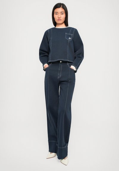 Sweatshirt court bleu marine avec des coutures blanches et une poche avant, associé à un pantalon large taille haute assorti et des chaussures pointues crème.