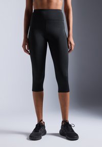Leggings Capri noirs taille haute fabriqués dans un matériau extensible, présentant une texture lisse et un design ajusté, se terminant juste en dessous du genou.