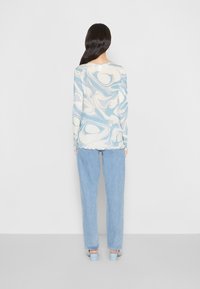 Maglietta a maniche lunghe con un motivo marmorizzato blu e bianco, abbinata a jeans a vita alta blu chiaro e tacchi blu chiaro; texture liscia.