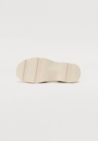 Light beige rubber shoe sole with textured grip, featuring three horizontal grooves and a rounded toe. Flat design, smooth finish.