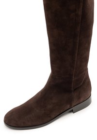 Stivale al ginocchio in camoscio marrone con una texture liscia, punta arrotondata e suola piatta in gomma. Caratterizzato da una cucitura laterale a scopo decorativo.