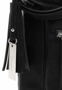 Černá kožená kabelka s hladkou texturou, s kovovým štítkem "SURI FREY" a ozdobnými černými třásněmi.