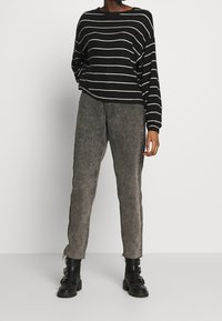 Schwarz-weißer gestreifter oversize Pullover, kombiniert mit grauen Jeans. Die Jeans haben einen geraden Schnitt und dezenten Seitendetails. Schwarze Ankle-Boots runden den Look ab.