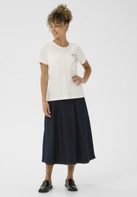 T-shirt en coton crème à manches courtes avec un graphique de cœur dessiné à la main ; associé à une jupe en denim foncé en ligne A et des mocassins noirs.