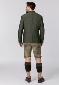 Green linen blazer with a single vent, paired with beige leather shorts, cable-knit leg warmers, and brown shoes.