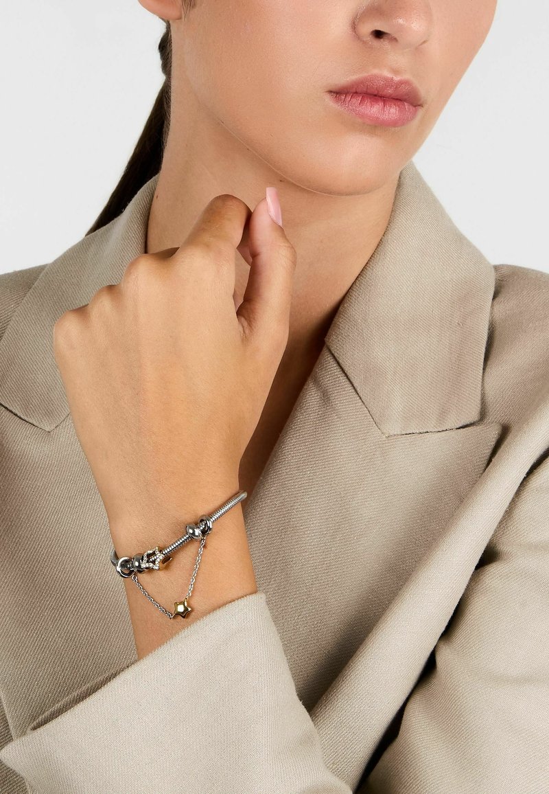 Bracciale in argento con ciondoli, caratterizzato da una catena con una stella dorata, perle lisce e decorazioni, indossato su un polso nudo.